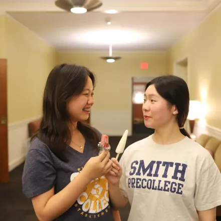 Two students smile at each other while holding popsicles.