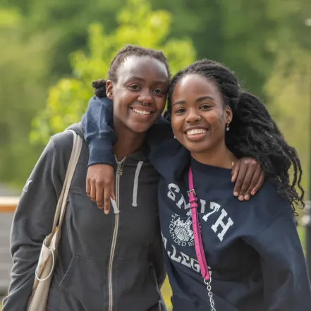 Two alums smiling with their arms around each other.