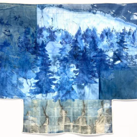 A T-shaped cyanotype textile tapestry in shades of indigo blue, featuring layered, silhouetted evergreen trees and a house against a snowy landscape, with a gridded lower section marked by muted gray and brown stains.