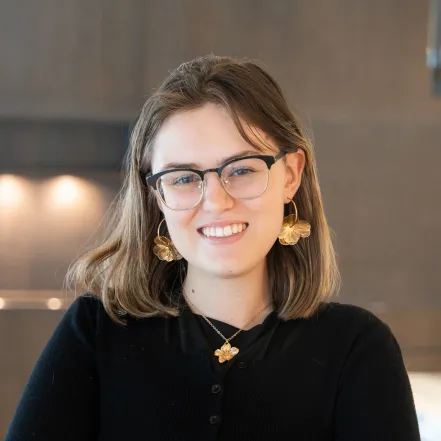 Headshot of Katherine Metzger wearing glasses, a black top, and gold flower jewelry.