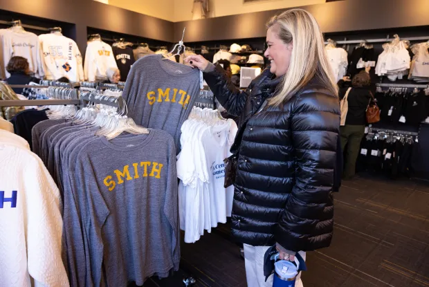 A woman holds up a Smith College T-shirt and smiles.