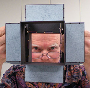 Daniel E. Kelm peering through one of his wire edge models, Metamorphic Book